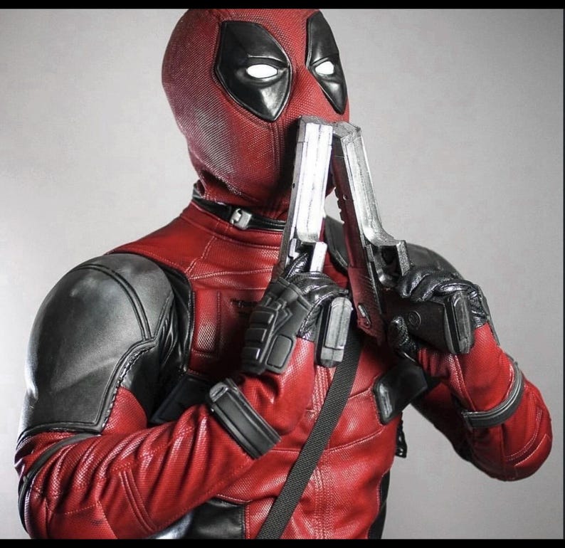 May include: A full-body costume featuring a textured red and black suit with a matching mask that has black eye patches and white lenses. The suit includes black gloves and shoulder armor, and the figure holds two silver metallic toy pistols.