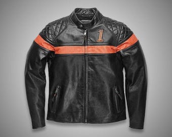 Puede incluir: Una chaqueta de moto de cuero negro con una franja horizontal naranja en el pecho, paneles acolchados en los hombros, cuello mao y un gráfico del número uno en el pecho izquierdo. La chaqueta incluye una cremallera frontal completa.