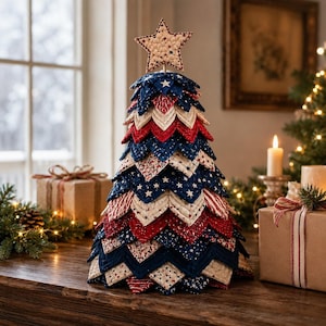 May include: A decorative tabletop Christmas tree constructed from layered, quilted fabric petals in red, white, and blue. The fabric features star and stripe patterns. A single quilted star sits at the peak of the tree, which is displayed on a wooden surface.