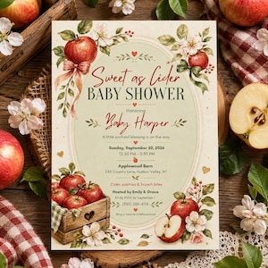 May include: A rectangular baby shower invitation card featuring a cream-coloured oval centre with red text reading Sweet as Cider BABY SHOWER Honoring Baby Harper, surrounded by watercolour illustrations of red apples, green leaves, and white blossoms.