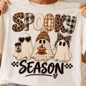 Puede incluir: Una camiseta color crema con el texto SPOOKY en letras estampadas sobre tres fantasmas. Un fantasma lleva gafas de sol de corazón y sostiene un café, otro lleva un gorro y sostiene una calabaza, y otro lleva un lazo de leopardo. Debajo aparece el texto SEASON.