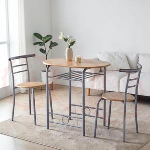 May include: A dining set consisting of an oval wooden table with a metal frame and two matching chairs. The table features a lower storage shelf and a light wood finish. The chairs have curved metal backrests and round wooden seats.