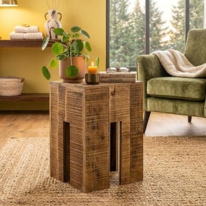 Könnte beinhalten: Ein quadratischer Beistelltisch aus Holz mit natürlicher Maserung und vertikalen Ausschnitten an jeder Seite. Auf der Tischplatte stehen eine grüne Pilea-Pflanze in einem Terrakottatopf, eine kleine gelbe Stumpenkerze und zwei Bücher mit den Titeln Wanderlust und Alpenstille.
