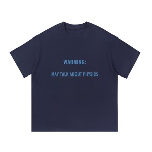 May include: A dark navy blue short-sleeved t-shirt with a crew neckline. The center of the chest features the text in a light blue sans-serif font that reads: WARNING: MAY TALK ABOUT PHYSICS. The garment has a standard fit and plain back.