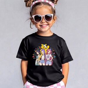 May include: A black short-sleeved t-shirt featuring a graphic print of three anime-style characters standing in front of a yellow bear figure, surrounded by a colourful array of small polka dots in shades of blue, orange, pink, and green.