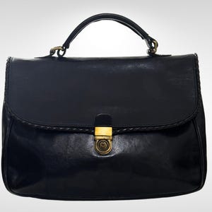 May include: A black leather handbag with a top handle and a flap closure. The bag features a gold-coloured clasp and decorative stitching along the edges. The bag is rectangular in shape.
