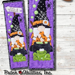 May include: A purple and black witch gnome with a cauldron and a frog, with the text "Toil & Trouble" on a sign above her. The gnome is wearing a black witch hat with a spider on it. The background is a purple fabric with black spiderwebs. The image is titled "October #10 of 12" and says "Skill Level: EASY".