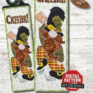 Op de afbeelding: Een digitaal patroon voor een gequilte wandhanger met een kabouter die een bierglas vasthoudt en een groene hoed, een geruite broek en een bruine baard draagt. De kabouter staat op een groene achtergrond met de tekst "Cheers!" en "March #3 of 12". Het patroon heet "Lucky Lewie" en maakt deel uit van de serie "Gnomes Thru the Year".