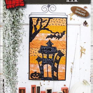 May include: A Halloween-themed quilt pattern featuring a spooky house with bats and a spiderweb design. The pattern is titled "Get Spooked" and is 30.5 cm by 45.7 cm. The skill level is beginner.