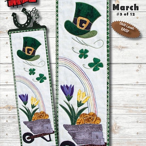 Puede incluir: Un patrón de acolchado para una pared colgante de 15,2 cm x 50,8 cm titulada "Breezy Blooms" que presenta un sombrero verde de duende, un arcoíris y una carretilla llena de flores. El patrón es parte de la "Monthly Minis #12 Series" y está etiquetado como "March #3 of 12". El nivel de habilidad se indica como "EASY".