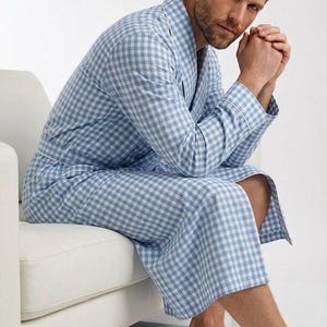May include: A light blue and white gingham patterned robe featuring a shawl collar, long sleeves with white piping trim, and a matching fabric tie belt. The garment is knee-length and constructed from a woven fabric with a classic checkered design.