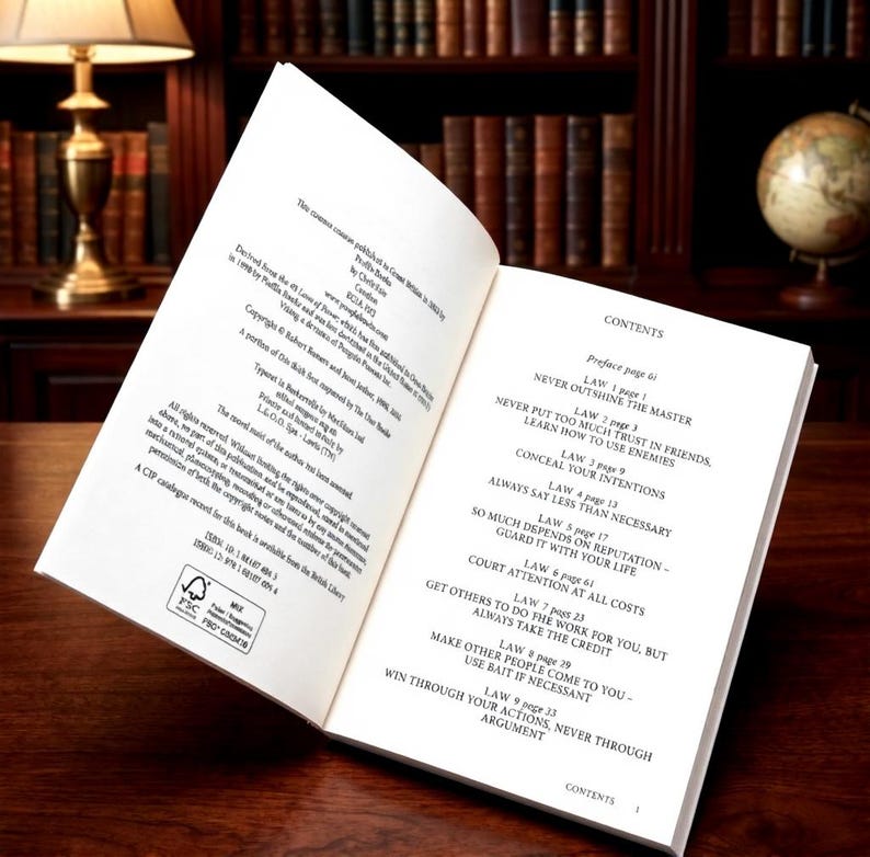 Pu&ograve; includere: Un libro con copertina rigida aperto con pagine bianche e testo nero. La pagina sinistra mostra le informazioni sul copyright e i dettagli di pubblicazione. La pagina destra mostra un indice che elenca nove leggi, tra cui Never Outshine the Master e Conceal Your Intentions.