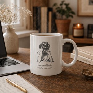 Peut inclure: Un mug en céramique blanche orné d'une illustration au trait noir représentant une personne la tête appuyée sur ses mains. Sous l'illustration, le texte indique : Born to read books. Forced to read emails. Le mug possède une anse courbée.