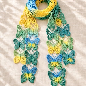May include: A long, open-work crochet scarf constructed from a series of interconnected butterfly motifs. The scarf features a vibrant gradient color scheme transitioning through shades of bright yellow, lime green, and deep teal blue throughout.