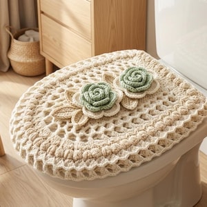 May include: A cream-colored crochet toilet seat cover featuring an openwork lattice pattern and two decorative three-dimensional sage green roses with beige leaves attached to the top surface of the cover.