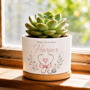May include: A white ceramic planter with a wooden base containing a green succulent. The planter features the text Happy Nurses Week and the name Harper, accompanied by a graphic of a stethoscope, a pink heart with a cross, and floral accents.