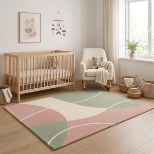 May include: A rectangular area rug featuring a geometric pattern of overlapping curved lines in muted sage green, dusty rose, and cream. The rug has a low-pile texture and covers a portion of the light-colored wooden floor in a nursery room.