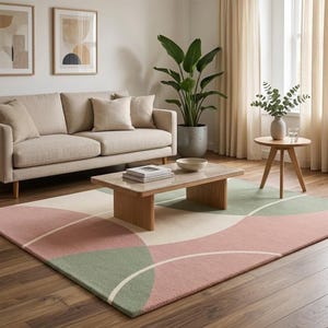 May include: A rectangular area rug featuring a geometric pattern of overlapping circles and arcs in muted sage green, dusty rose pink, and cream. The rug has a low-pile texture and covers a portion of the dark wood floor beneath a wooden coffee table.