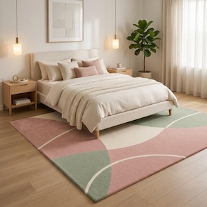 May include: A rectangular area rug featuring a geometric pattern of large, overlapping circles in muted sage green, dusty rose, and cream. The rug has a low-pile texture and is positioned on a light-toned wooden floor beneath a bed with neutral bedding.