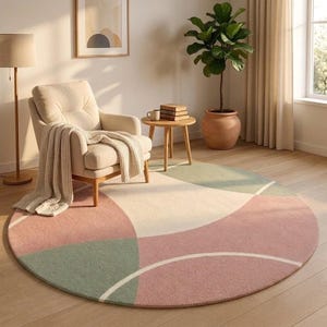 May include: A large circular area rug featuring a geometric pattern of soft pink, sage green, and cream-colored segments separated by thin white curved lines. The rug has a textured, plush surface and is positioned on a light-toned wooden floor.