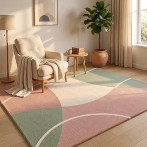 May include: A rectangular area rug featuring a geometric pattern of overlapping circles and curved segments in muted shades of dusty pink, sage green, and cream. The design is composed of soft, textured fibers with clean white lines defining the shapes.