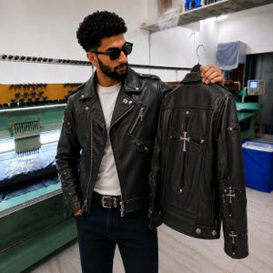 May include: A black leather motorcycle jacket featuring silver-toned cross hardware on the back and sleeves, a notched lapel, asymmetrical zipper closure, and multiple zippered pockets. The jacket is displayed alongside a matching leather jacket.