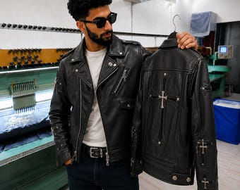 May include: A black leather motorcycle jacket featuring silver-toned cross hardware on the back and sleeves, a notched lapel, asymmetrical zipper closure, and multiple zippered pockets. The jacket is displayed alongside a matching leather jacket.