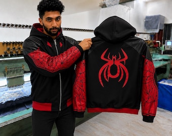 May include: A black and red zip-up hoodie featuring a large red spider emblem on the back. The sleeves display a black web pattern over a red background, while the hood and main body are black with red accents at the hem and inner lining.
