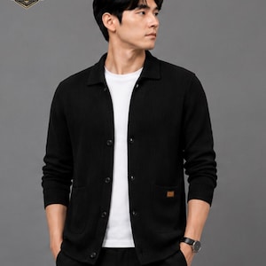 May include: A black long-sleeved button-down cardigan with a ribbed texture, a collar, and two front pockets. The garment features a small brown rectangular patch on the lower left pocket and is worn over a plain white t-shirt. The Titanapex logo is visible.