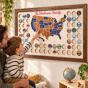 May include: A wooden wall-mounted map of the United States featuring the text The Workman Family, with brown and blue state cutouts and circular slots for round tokens depicting various national parks and landscapes.