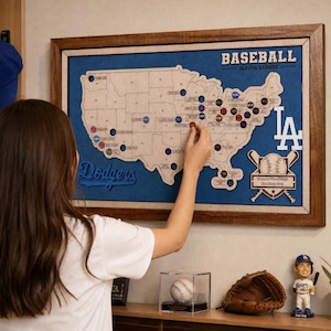 Puede incluir: Un mapa de madera enmarcado de los Estados Unidos con ubicaciones de estadios de béisbol, el texto BASEBALL MAJOR LEAGUE, Dodgers y un logo LA. El mapa incluye recortes circulares para marcadores y un gráfico de bates cruzados.