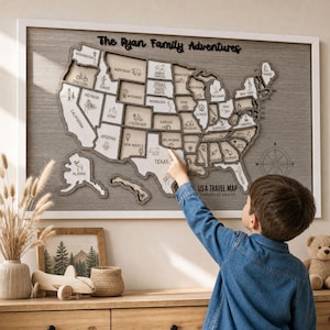 Pode incluir: Um mapa de parede de madeira dos Estados Unidos emoldurado com o texto The Ryan Family Adventures e USA TRAVEL MAP ADVENTURE AWAITS. Cada estado é cortado individualmente com ícones gravados representando marcos e vida selvagem.
