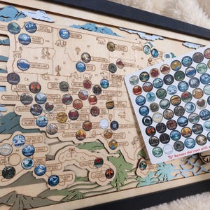 May include: A layered wooden map of the United States featuring engraved state outlines and national park locations. Circular stickers depicting various landscapes are placed on the map, with a sheet of matching stickers included in the foreground.