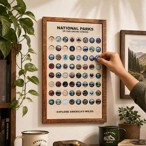 Puede incluir: Un expositor de pared rectangular con marco de madera titulado NATIONAL PARKS OF THE UNITED STATES, que presenta una cuadrícula de huecos circulares para fichas redondas. El texto EXPLORE AMERICA'S WILDS aparece en la base del panel claro.