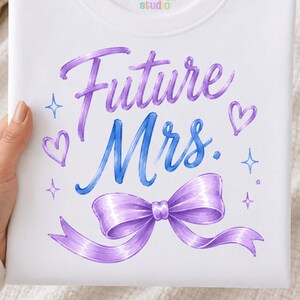 May include: A white crewneck sweatshirt featuring the purple and blue text Future Mrs. with a purple ribbon bow graphic, small hearts, and star accents. The interior neck label displays the text Kreate4u studio in colourful lettering.