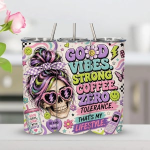 May include: A cylindrical tumbler with a metal straw featuring a skull wearing heart-shaped glasses and a checkered headband. The design includes colorful graphics of flowers, smiley faces, a flip phone, and the text GOOD VIBES STRONG COFFEE ZERO TOLERANCE THAT'S MY LIFESTYLE.