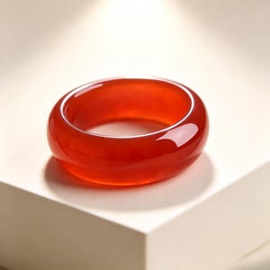 Puede incluir: Un anillo de banda liso y pulido, elaborado con piedra cornalina roja, vibrante y translúcida. El anillo presenta un perfil grueso y redondeado con un acabado brillante que refleja la luz, mostrando el tono rojo anaranjado profundo y uniforme.