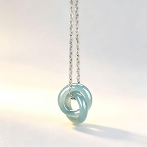 Può includere: Una collana con una catena in metallo color argento e due pendenti circolari intrecciati, lisci e di colore azzurro. I pendenti hanno una finitura lucida e traslucida e sono sospesi verticalmente alla catena, creando un design circolare.
