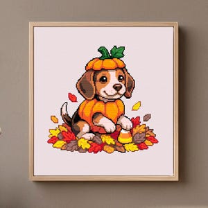 Könnte beinhalten: Ein quadratisch gerahmtes Kreuzstichmuster mit einem Pixel-Art-Beagle-Welpen in einem Kürbiskostüm. Der Welpe sitzt inmitten eines Haufens bunter Herbstblätter in Rot-, Gelb- und Brauntönen, daneben liegt ein einzelnes Stück Zuckermais.