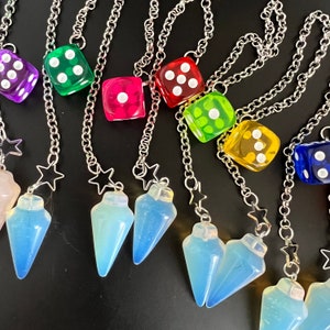 May include: A set of seven colorful dice charms with silver chains and blue crystal pendulum charms. The dice are in various colors, including red, green, yellow, blue, and purple. The charms are attached to silver chains and have a star-shaped charm at the top.