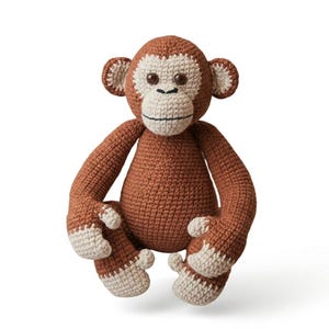 May include: A handcrafted crochet monkey toy featuring a brown body with cream-coloured accents on the face, ears, hands, and feet. The stuffed animal has dark brown safety eyes, a stitched black mouth, and a textured yarn construction throughout.