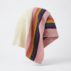 May include: A knitted blanket featuring a large cream-colored section on one side and a series of vertical stripes in shades of pink, yellow, green, and dark purple on the other side. The textile has a consistent garter stitch texture throughout.