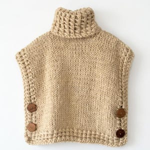 May include: A sleeveless beige knit sweater featuring a high turtleneck collar and a chunky textured weave. The garment includes two dark brown circular wooden buttons on each side seam, providing a functional closure detail along the lower edges.