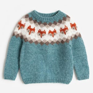 May include: A teal long-sleeve knit jumper featuring a round neckline and a yoke pattern. The yoke displays a repeating geometric design in white, brown, and orange, with stylised orange fox motifs integrated into the white section of the knit.