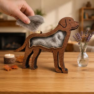 Peut inclure: Une boîte vitrée en bois brun foncé en forme de chien, contenant des poils gris derrière une paroi transparente. Un petit cœur en bois est fixé sur le dos du chien. L'objet représente un chien debout avec une queue et quatre pattes.