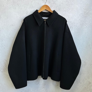 May include: A black zip-up jacket with a pointed collar, long sleeves, and two side pockets. The garment features a central zipper closure and a white interior label with the text Acne Studios, hanging on a wooden hanger against a textured wall.