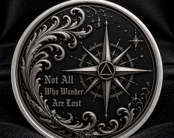 Könnte beinhalten: Eine kreisförmige Münze aus silberfarbenem Metall mit einem geprägten Kompassrosen-Design, filigranen Schnörkeln und dem eingravierten Text "Not All Who Wander Are Lost" auf dunklem Hintergrund, präsentiert in einer schwarz ausgekleideten Box.