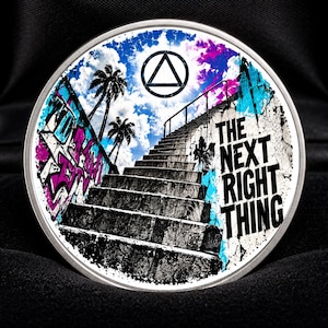 Op de afbeelding: Een ronde medaille met een afbeelding van een trap die omhoog leidt onder een blauwe lucht met palmbomen. Het ontwerp bevat een zwart driehoekssymbool bovenaan en de tekst THE NEXT RIGHT THING in dikke zwarte letters aan de rechterkant.