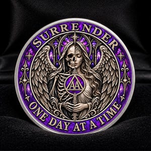 Könnte beinhalten: Eine kreisförmige, silberfarbene Medaille mit einer Figur mit geteiltem Gesicht, halb Skelett und halb Mensch, mit Flügeln sowie dem Text SURRENDER und ONE DAY AT A TIME. Die Mitte zeigt ein AA-Symbol in einem Dreieck vor violettem Glas.