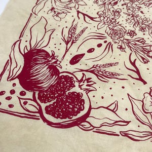 May include: A cream-colored fabric with a red floral and fruit design. The design includes pomegranates, wheat stalks, and flowers.